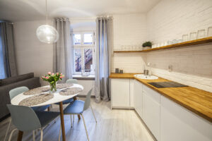 salon z białym aneksem kuchennym, okrągły stolik z kwiatami