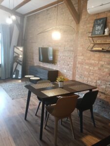 Stół jadalny z czterema krzesłami i doniczką, ceglana ściana, wisząca lampa i telewizor